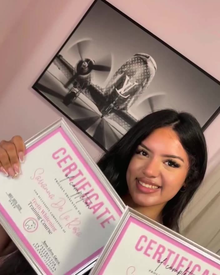 A graduate holding two pink training certificates